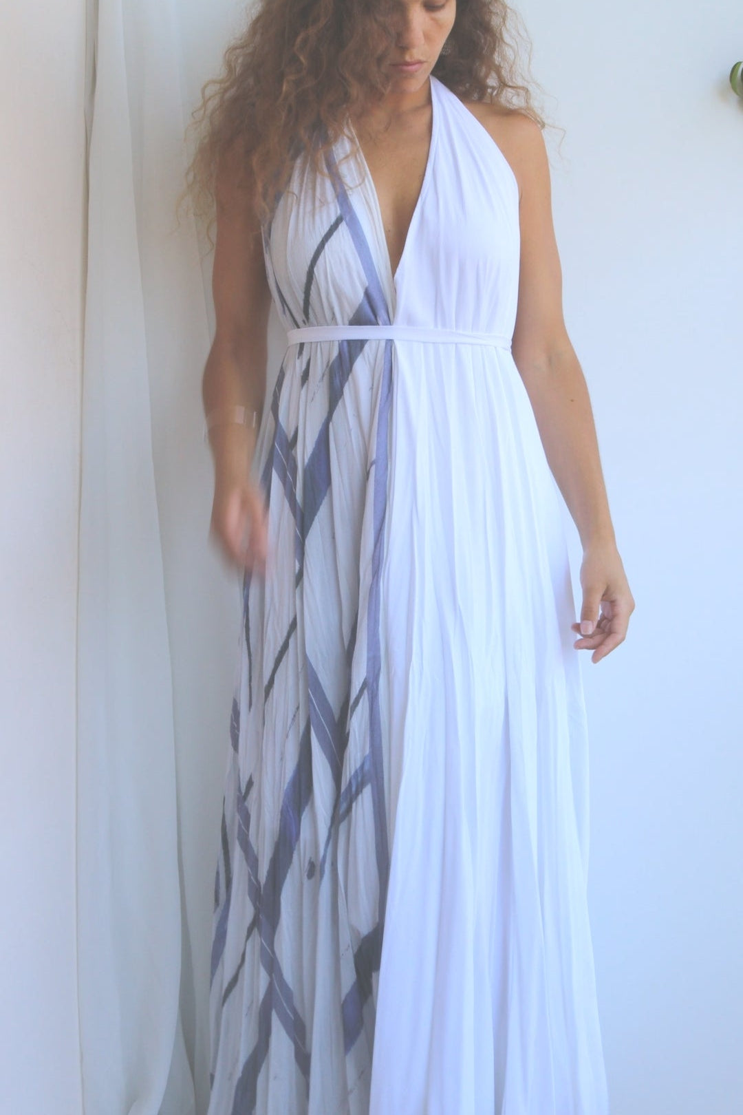 Woman wearing a white dress with a blue abstract pattern, standing against a plain background.